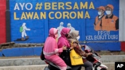 Perempuan muslim mengendarai motor di depan mural bertema virus corona di Jakarta (dok: AP)