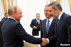ولادیمیر پوتین، رئیس جمهوری روسیه، در حال دست دادن با هاکان فیدان، رئیس دستگاه اطلاعاتی ترکیه و خلوصی آکار وزیر دفاع ترکیه (در سمت راست هاکان فیدان). کاخ کرملین، ۲۴ اوت ٢٠١٨