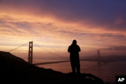 Jeunne Victorino, visiting from San Diego, photographs the sunrise and the Golden Gate Bridge from the Marin Headlands Tuesday, Jan. 17, 2017, in San Francisco. (AP Photo/Marcio Jose Sanchez)