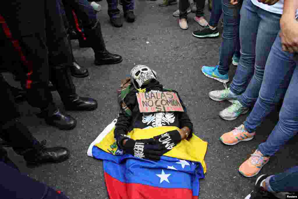 An opposition supporter wearing a costume and a placard that reads "Bullets no, food yes" lies on the floor in front of riot policemen during a rally against President Nicolas Maduro's government in Caracas, Venezuela.