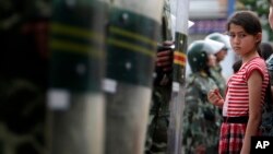 Uyg'ur qiz Xitoy harbiy politsiyachilari paradini tomosha qilmoqda, Urumchi, Shinjon, 2009-yil, 9-iyul