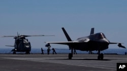 資料照 - 英國航母伊麗莎白女王號上的機械師正給一架停留在甲板上的直升機加油，旁邊一架F-35隱身戰機準備起飛。