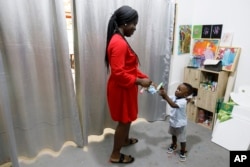 Chantelle Kuukua Eghan, 25, gives paint to her son Ace-Liam Nana Sam Ankrah, who will turn two in July, at her mother's art gallery in Accra, Ghana, Monday, May 27, 2024. (AP Photo/Misper Apawu)