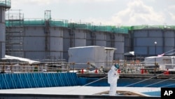 A worker, wearing protective suits and masks, takes notes in front of storage tanks for radioactive water at the Fukushima Dai-ichi nuclear power plant in Okuma, Fukushima Prefecture.