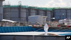 FILE - A worker, wearing protective suits and masks, takes notes in front of storage tanks for radioactive water at the tsunami-crippled Fukushima Dai-ichi nuclear power plant, operated by Tokyo Electric Power Co. (TEPCO), in Okuma, Fukushima Prefecture. 