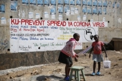 Two young girls sell groundnuts in front of an informational mural advising on precautions to avoid catching the new coronavirus, in the Kibera slum, or informal settlement, of Nairobi, Kenya Thursday, April 2, 2020.