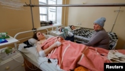 Una conocida visita un hospital y se sienta junto a Marina Klimenko, de 28 años, y Lyudmila Antonenko, de 46, trabajadoras heridas en un mercado que recientemente fue atacado por bombardeos en Donetsk, Ucrania, controlada por Rusia, 22 de enero de 2024. 