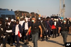 FILE - Italian border police officers escort sub Saharan men on their way to a relocation center, after arriving aboard the Golfo Azzurro rescue vessel at the port of Augusta, in Sicily, Italy, June 23, 2017.