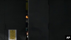 Una empleada con tapabocas de una tienda de electrónica mira desde la entrada del establecimiento mientras espera que lleguen los clientes, en Caracas. Agosto 29, 2020.