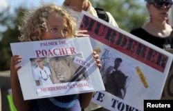 Protesters hold signs during a rally outside the River Bluff Dental clinic against the killing of a famous lion in Zimbabwe, in Bloomington, Minnesota, July 29, 2015.