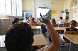 A protective facemask is seen on the hand of a student raising his arm during class at the Carl Orff primary school in west Berlin on August 10, 2020, as school resumed after the summer break in Berlin and several other German states amid a Coronavirus Co