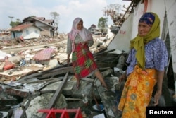Seorang perempuan Aceh dan ibunya mencari barang milik keluarganya dari tengah puing-puing rumahnya yang rusak akibat tsunami di Banda Aceh, 2005. (Foto: Reuters)