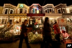 In this Dec. 10, 2012 photo, people walk past holiday decorations on homes on 34th Street in the Hampden neighborhood of Baltimore.