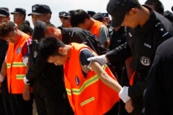 រូបឯកសារ៖ ជនជាតិចិនក្នុង​ឯកសណ្ឋានអាវពណ៌ទឹកក្រូច ត្រូវបានចាប់ខ្លួន​ និង​បញ្ជូន​ទៅ​ប្រទេសចិនវិញ ដោយ​មន្ត្រីប៉ូលិសចិន មុនពេលពួកគេឡើងយន្តហោះចេញពីអាកាសយានដ្ឋានអន្តរជាតិភ្នំពេញនៃប្រទេសកម្ពុជា កាលពីថ្ងៃទី១២ ខែតុលា ឆ្នាំ២០១៧។