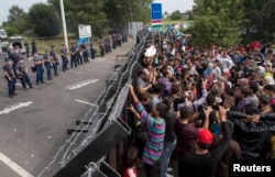 Migrants stand in front of a barrier at the border with Hungary near the village of Horgos, Serbia, Sept. 16, 2015.