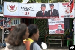 FILE - A couple rides a motorcycle past a campaign banners for Indonesian presidential candidate Prabowo Subianto, left, and his running mate Sandiaga Uno in Jakarta, Indonesia, Jan. 17, 2019.