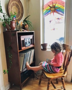In this April 2, 2020, photo provided by Cassy Quinlan, 4-year-old Polly Fraley listens in Homer, Alaska, to children's stories being read on air at local radio station KBBI by librarian Claudia Haines.