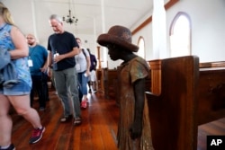 FILE - In this July 14, 2017 file photo, visitors file past the sculpture of a slave girl, one out of 40 statues spread about the grounds, titled, "Children of Whitney," by Woodrow Nash, inside the Antioch Baptist Church