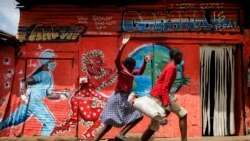 Children run down a street past an informational mural warning people about the dangers of coronavirus in the Kibera slum of Nairobi, Kenya on Wednesday, June 3, 2020.