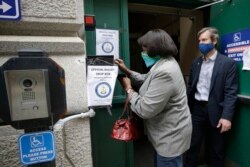 FILE - A voter, left, places a ballot in a secure box as Providence City Clerk Shawn Selleck, right, looks on, Tuesday, June 2, 2020, in Providence, R.I. More American voters asked for mail ballots during the coronavirus outbreak.