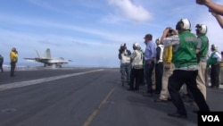 U.S. Secretary of Defense Ash Carter (center, in blue shirt) watches a jet take off from the USS John C. Stennis in the South China Sea (C.Babb/VOA). Carter says the U.S. is strengthening its military role in the region but is not aiming to provoke anything.