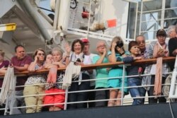 អ្នកដំណើរតាមនាវា Westerdam ឈរមើលការចាកចេញរបស់អ្នកដំណើរមួយចំនួន កាលពីព្រឹកថ្ងៃសុក្រ ទី១៤ ខែកុម្ភៈ ឆ្នាំ២០២០។ (ស៊ុន ណារិន/VOA)