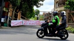 Ojek online melintas di gerbang kampung yang ditutup. Covid-19 berdampak besar pengemudi ojol. (Foto: VOA/Nurhadi)
