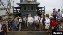 Myanmar government officials and U.N. officials stand on a boat used for human trafficking at a jetty outside Sittwe, Myanmar.