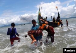 Smoke is seen on Myanmar's side of border as an exhausted Rohingya refugee woman is carried to the shore after crossing the Bangladesh-Myanmar border by boat through the Bay of Bengal, in Shah Porir Dwip, Bangladesh September 11, 2017.