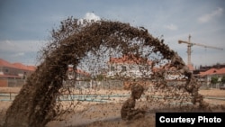 March 27, 2009 - Phnom Penh, Cambodia. A child plays in muddy water that is spraying out of a broken pipe, the pipes are pumping sand into a natural lake in Borei Reakreay community. The community was evicted from their homes in mid-2009 to make way for r