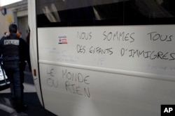 France Migrants: Police officer walks by a graffiti reading "We Are All Migrants' Children, The World or Nothing" after they evacuate migrants camped out in the empty Jean Jaures school in northeast Paris, France, Wednesday, May 4, 2016.