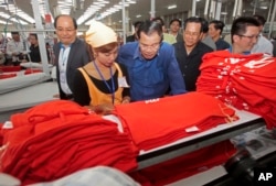 In this file photo taken on Aug. 30, 2017,Prime Minister Hun Sen, center, leans over a garment worker during a visit to a factory outside of Phnom Penh, Cambodia.