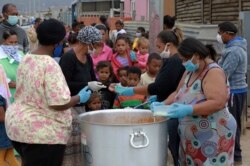 Children line up for food at a feeding scheme in Lavender Hill, Cape Town South Africa, Tuesday, April 21, 2020, during the fourth week of lockdown to contain the spread of coronavirus. (AP Photo/Nardus Engelbrecht)