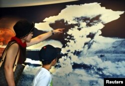 FILE - A mother and son look at a picture of the mushroom cloud atomic bomb blast as they visit Hiroshima Peace Memorial Museum in Hiroshima, Aug. 5, 2002. The bomb dropped on Hiroshima virtually leveled the entire city.