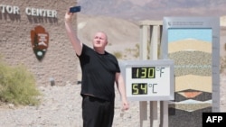 Scott Hughes, turis dari Swansea, Wales, Inggris, berswafoto di samping layar digital yang menunjukkan suhu udara 54 Celsius, selama gelombang panas di Taman Nasional Death Valley di California, 16 Juli 2023.