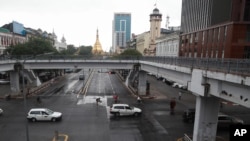 Vehicles make their ways as pedestrians cross a road with Sule pagoda seen the in background in downtown Yangon, Myanmar, Monday, July 19, 2021. (AP Photo/Thein Zaw)