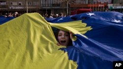Arhiva -- Devojka proviruje kroz džinovsku zastavu Kosova tokom proslave kosovkse nezavisnosti, u Prištini, 17. februara 2008.