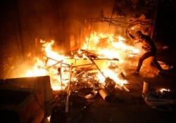 An anti-government protester tries to extinguish a tent which was set on fire by civilian men believed to be the private unit of the parliament guards, during ongoing protests against the political elites, in Beirut, Lebanon, Jan. 18, 2020.