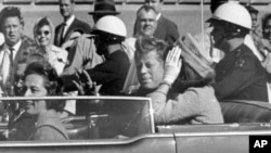 ARCHIVO - El presidente John F. Kennedy saluda desde su automóvil en una caravana aproximadamente un minuto antes de que le dispararan, el 22 de noviembre de 1963, en Dallas, Texas.