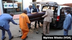 Des employés de Sopema Funerals chargent le corps d'une personne décédée dans un corbillard à Soweto, en Afrique du Sud, le 4 août 2020.