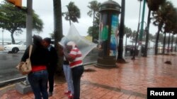 មនុស្ស​ម្នា​ឈរ​នៅ​ក្រោម​ទឹក​ភ្លៀង​នៅ​លើ​ផ្លូវ​ដើរ​មួយ​ក្នុង​ក្រុងSanto Domingo នៃ​ប្រទេស​ដូមីនីក (Dominica)។