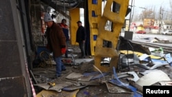 Orang-orang membantu membersihkan puing-puing di stasiun bus yang rusak setelah penembakan, di tengah serangan Rusia di Ukraina, di Kherson, Ukraina 21 Februari 2023. (Foto: REUTERS/Lisi Niesner)
