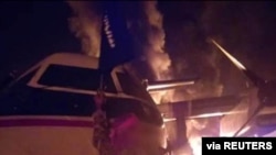 FILE - An image distributed by al-Shabab after an attack on a military base in Kenya shows a militant holding the group's flag next to a burning aircraft, said to be at the Manda Bay Airfield in Manda, Lamu, Kenya, Jan. 5, 2020.