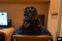 Emily Hollenbeck, a deep brain stimulation therapy patient, demonstrates an EEG device that records brain activity as she reacts to short videos at Mount Sinai’s “Q-Lab” in New York on Dec. 20, 2023. (AP Photo/Mary Conlon)
