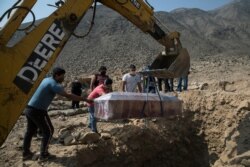 A backhoe places the coffin containing the body of Marina Salazar, 75, who died from COVID-19 complications, into her tomb at a cemetery in Carabayllo, Lima, Peru, Aug. 13, 2020.