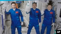 A screen grab taken at Beijing Aerospace Control Center in Beijing, China, Oct. 16, 2021, and released by Xinhua News Agency, shows three Chinese astronauts waving after they entered China's Tiangong space station core module Tianhe. 