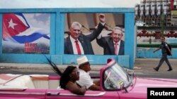 Un automóvil antiguo pasa junto a una imagen del expresidente de Cuba, Raúl Castro, y del presidente y primer secretario del Partido Comunista de Cuba, Miguel Díaz-Canel, junto a un cartel que dice: "Somos continuidad", en La Habana, Cuba, el 17 de abril de 2023.