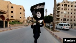 FILE - A man waves an Islamic State flag on the streets of Raqqa, Syria, in 2014. German authorities have arrested a Syrian doctoral student in Darmstadt; he's suspected of promoting IS and its symbols on social media.