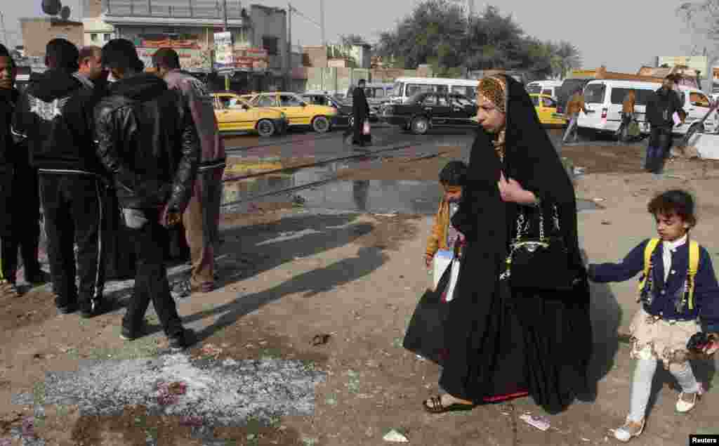 A woman and her children walk past the site of a suicide bombing in the Shi'ite neighborhood of Kadhimiya in Baghdad, Feb. 9, 2015.