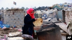 Umm Salem bakes bread in front of her hut at an encampment for the displaced outside Baghdad, Iraq, Feb. 12, 2018. 
